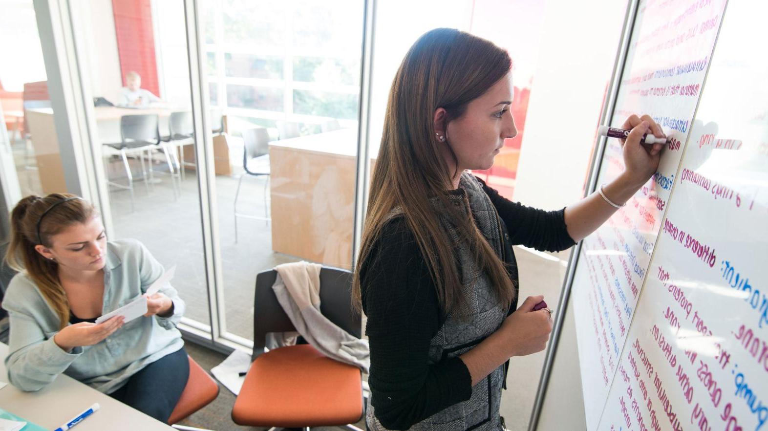 A female student takes notes on the white boards in the learning commons